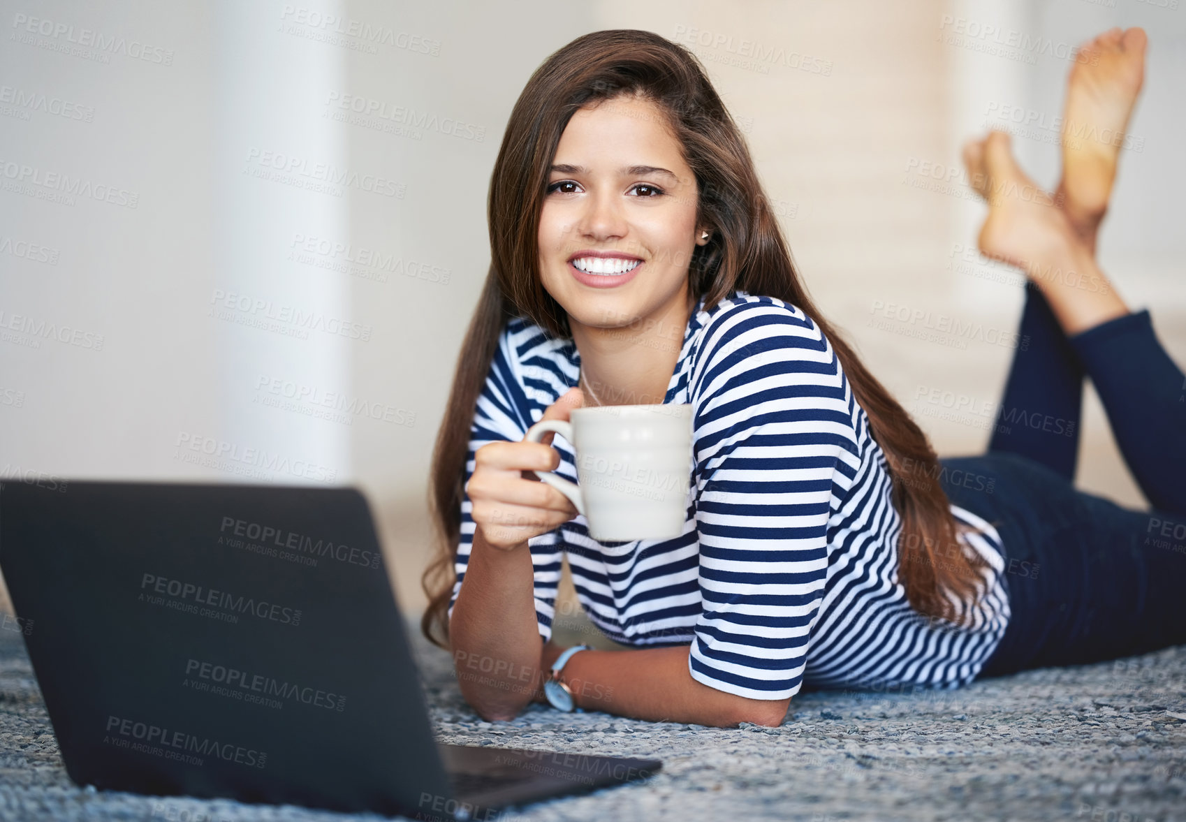 Buy stock photo Portrait of a smiling young woman lying on the floor at home using a laptop