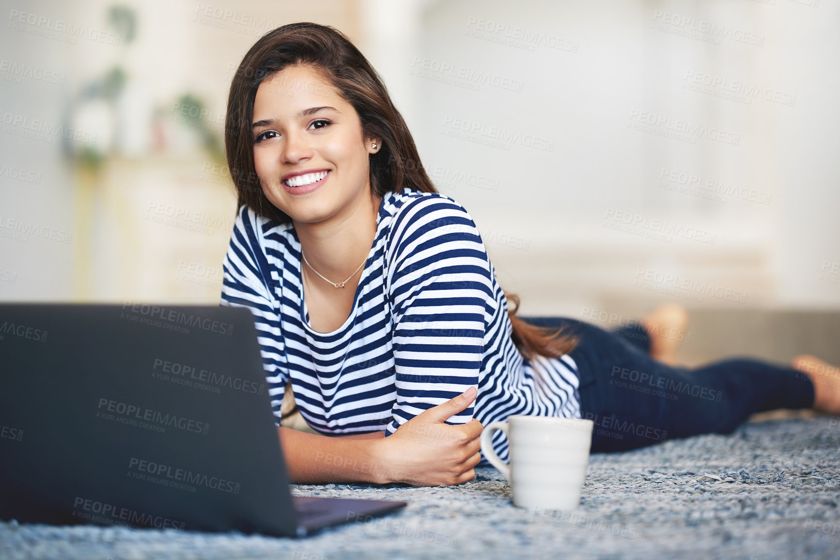 Buy stock photo Portrait of a smiling young woman lying on the floor at home using a laptop