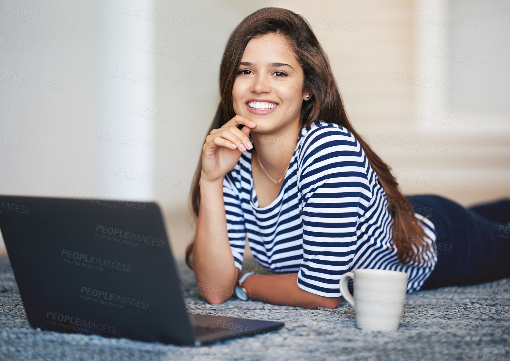 Buy stock photo Portrait of a smiling young woman lying on the floor at home using a laptop