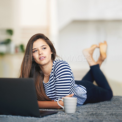 Buy stock photo Shot of a young woman lying on the floor at home using a laptop deep in thought