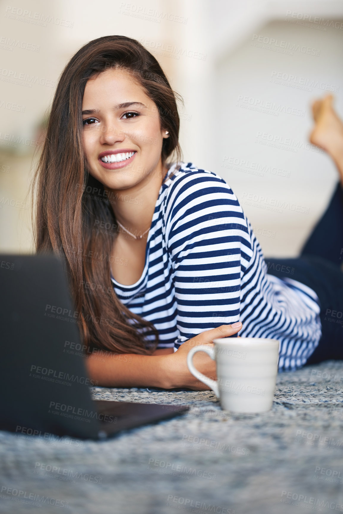 Buy stock photo Portrait of a smiling young woman lying on the floor at home using a laptop