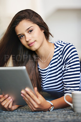 Buy stock photo Portrait of a smiling young woman lying on the floor at home using a digital tablet