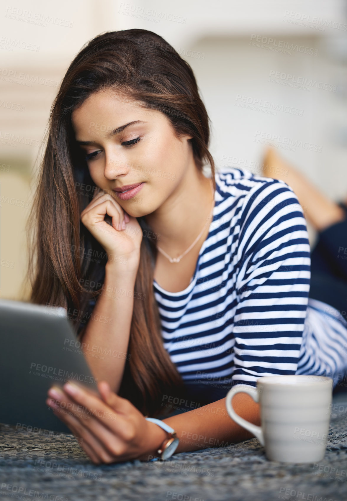 Buy stock photo Shot of a young woman lying on the floor at home using a digital tablet