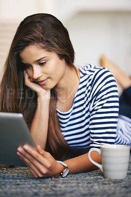 Buy stock photo Shot of a young woman lying on the floor at home using a digital tablet