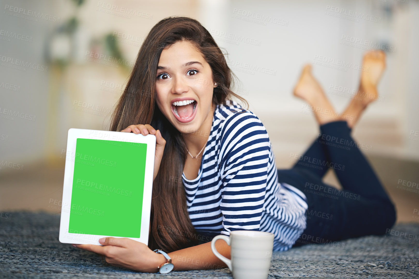 Buy stock photo Portrait of an ecstatic young woman lying on the floor at home holding up a digital tablet with a chroma key screen