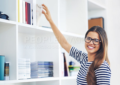Buy stock photo Portrait of a smiling young woman reaching for a book on a shelf at home