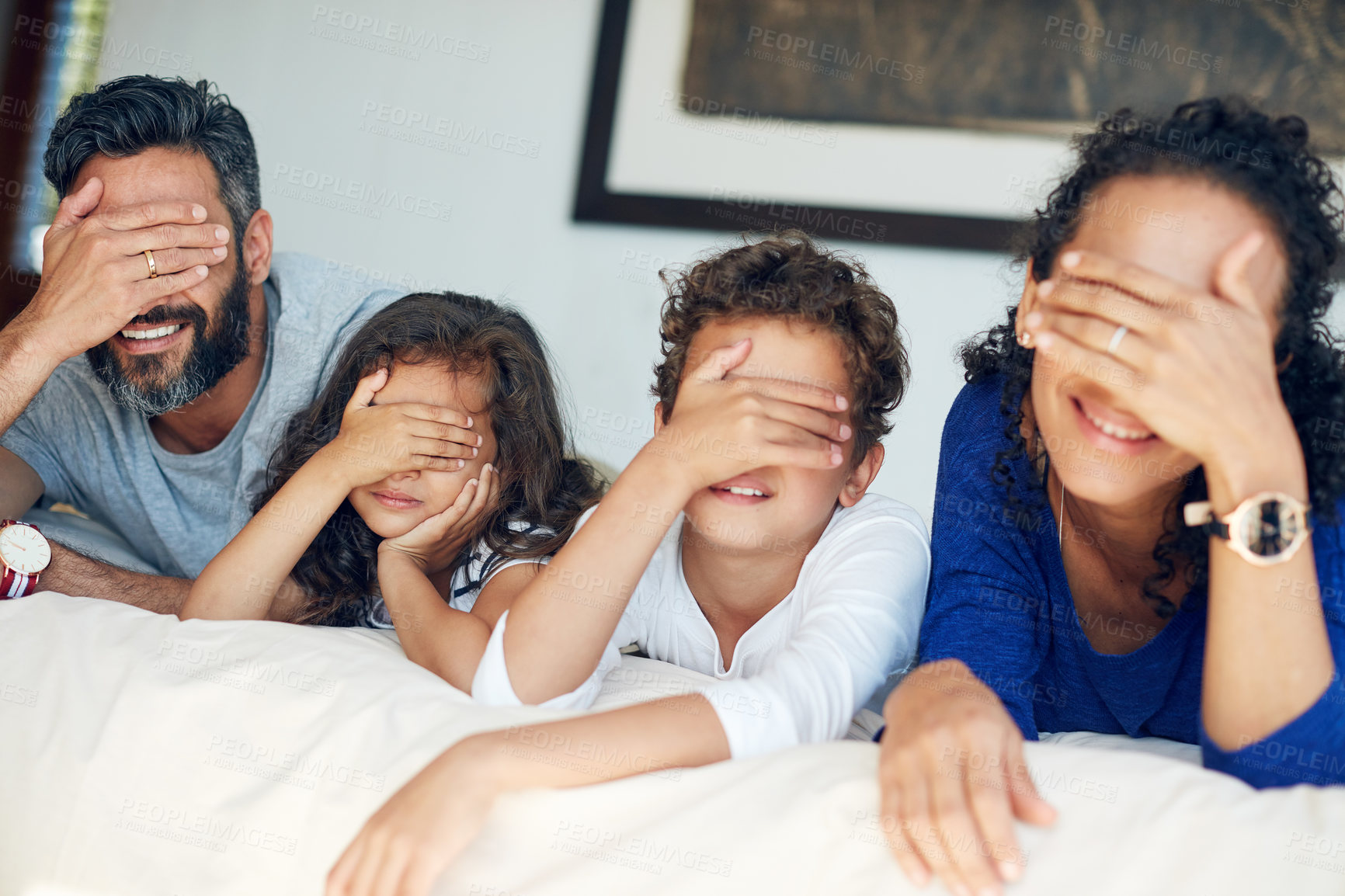 Buy stock photo Cropped shot of a family covering their eyes while lying down on a bed at home