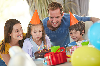 Buy stock photo Shot of a little girl blowing out the candles of her birthday cake surrounded by her family