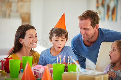 Buy stock photo Shot of a little boy blowing out the candles of his birthday cake surrounded by his family