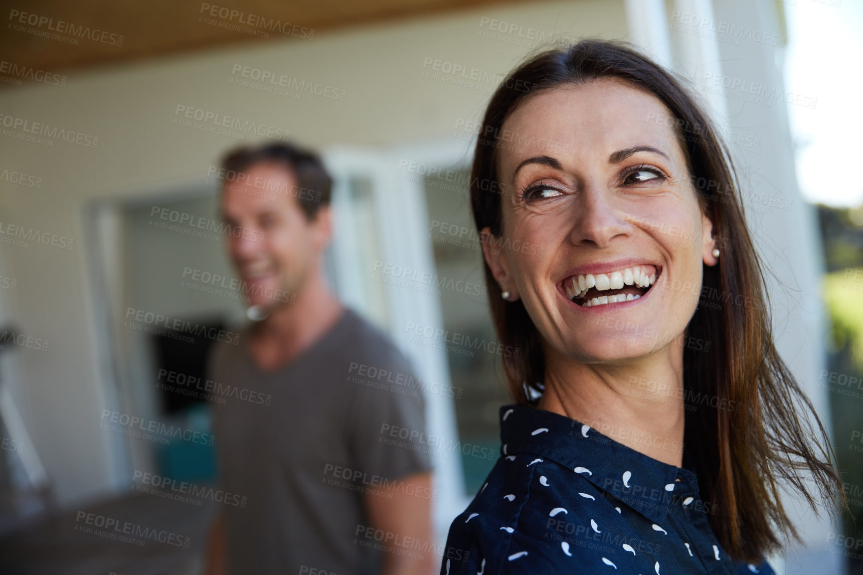 Buy stock photo Shot of a woman laughing with her husband blurred in the background