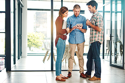 Buy stock photo Full length shot of three young coworkers talking while looking at a digital tablet