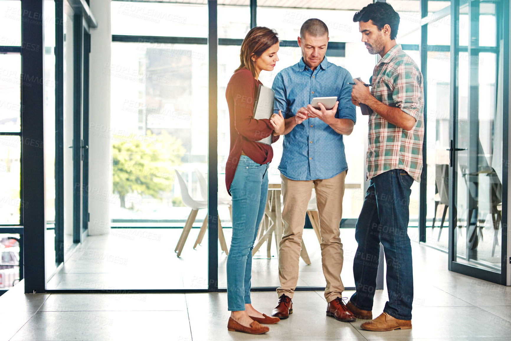 Buy stock photo Full length shot of three young coworkers talking while looking at a digital tablet