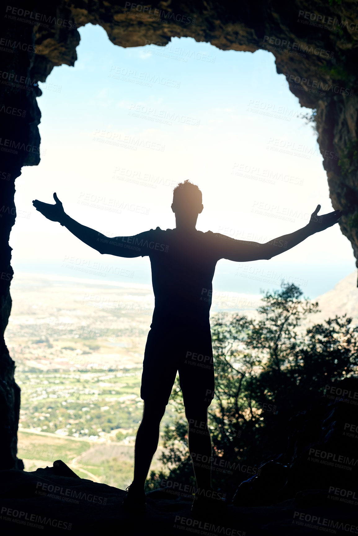 Buy stock photo Rearview shot of a young man standing at the top of a mountain with his arms outstretched