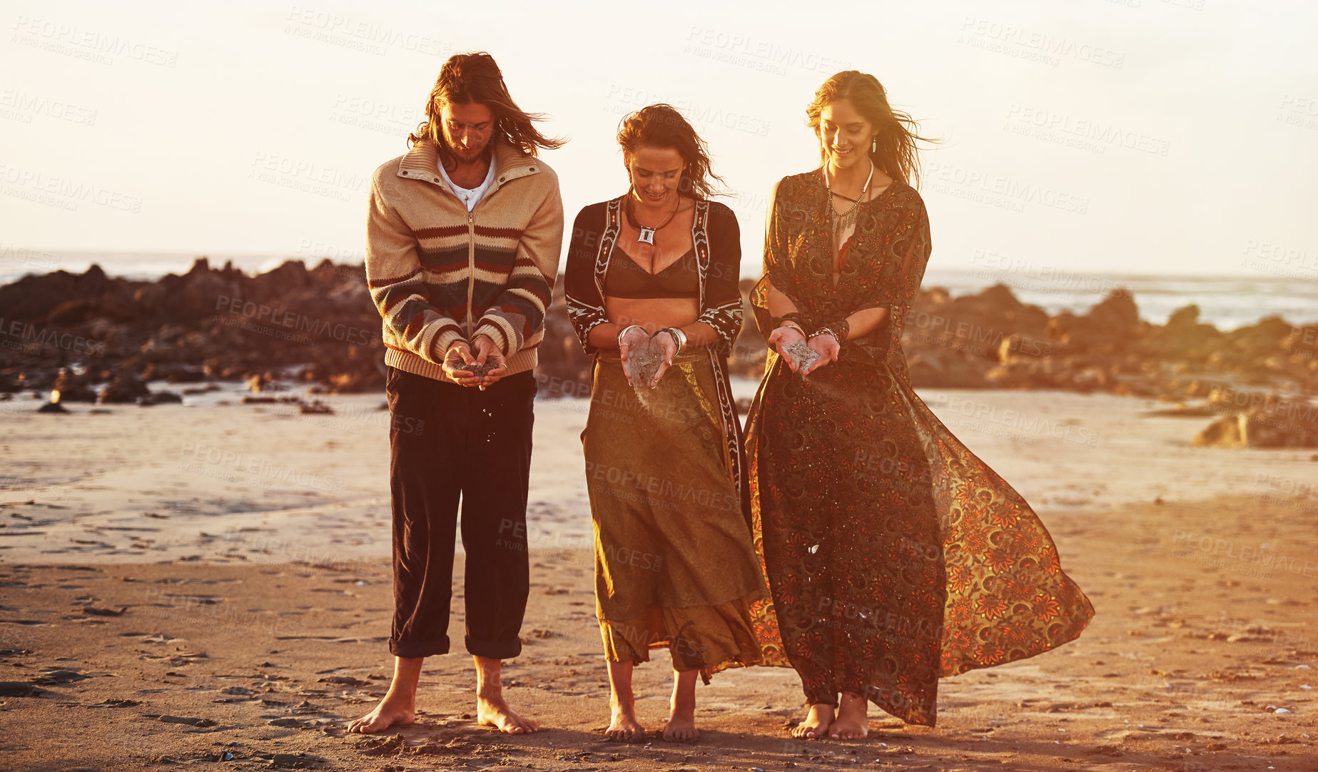 Buy stock photo Shot of three gypsies holding sand in their hands on the beach