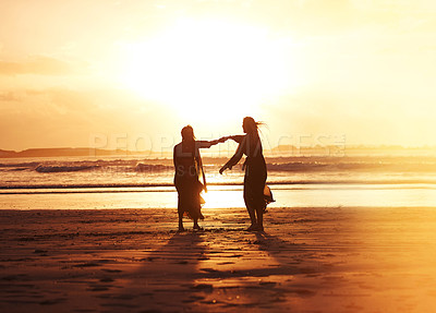 Buy stock photo Shot of two young women spending the day at the beach at sunset