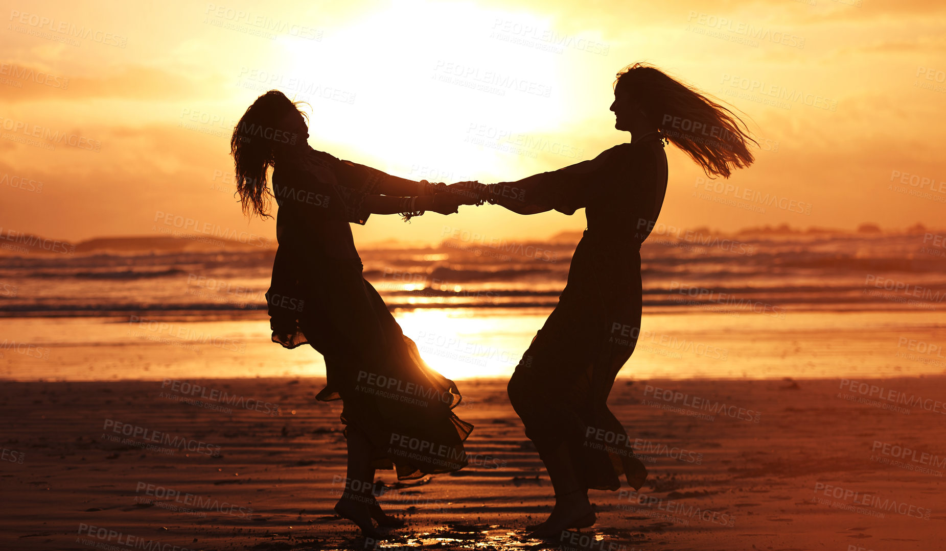 Buy stock photo Shot of two young women spending the day at the beach at sunset