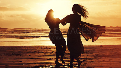 Buy stock photo Shot of two young women spending the day at the beach at sunset