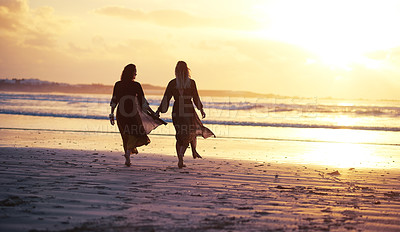 Buy stock photo Shot of two young women spending the day at the beach at sunset