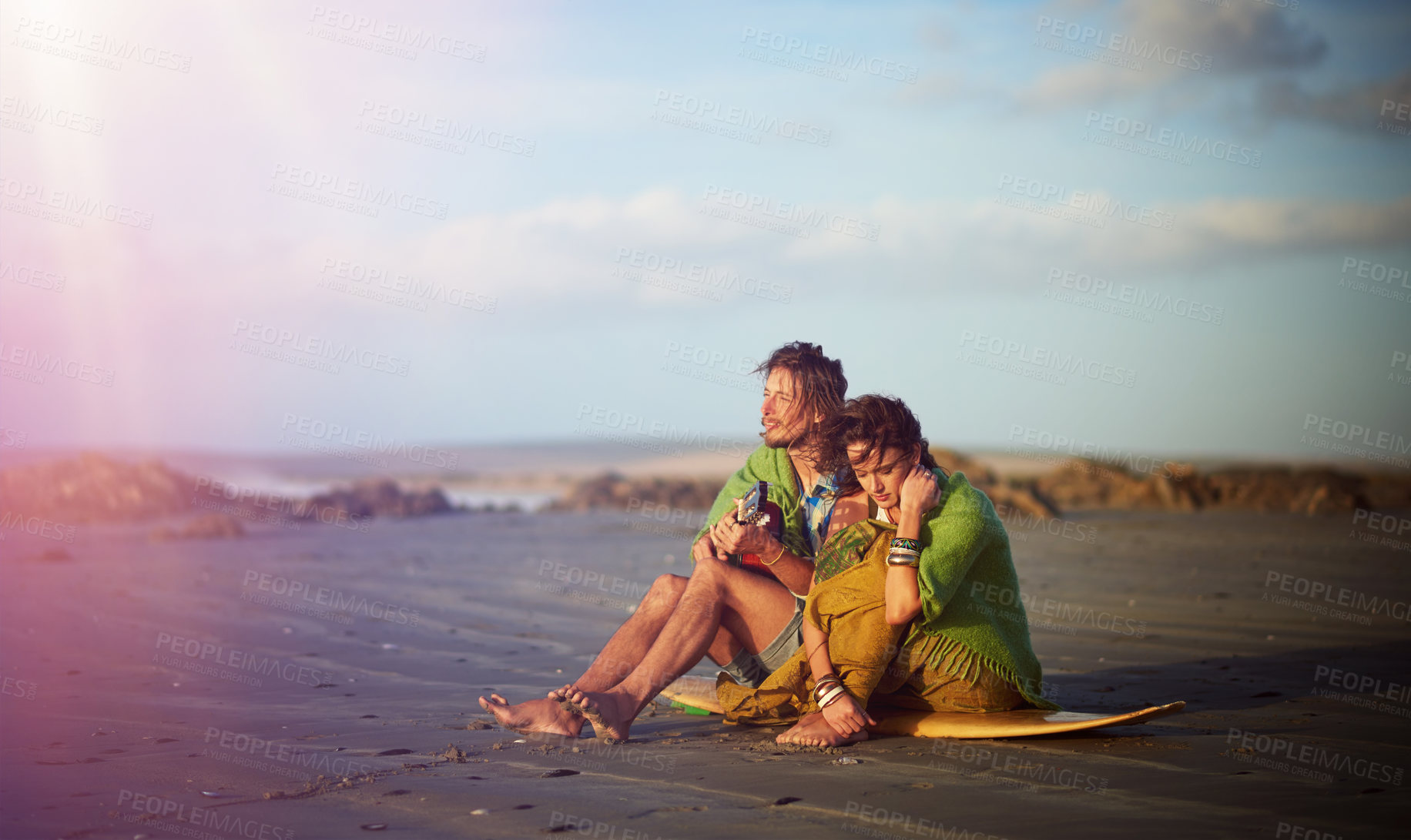 Buy stock photo Shot of a young man playing the guitar while sitting on the beach with his girlfriend