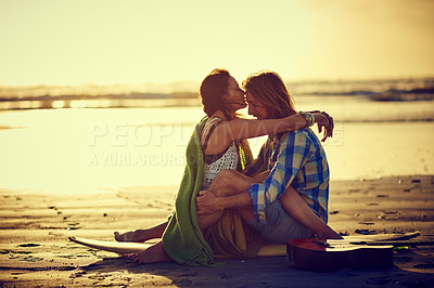Buy stock photo Shot of a couple sitting on the beach with their legs intertwined