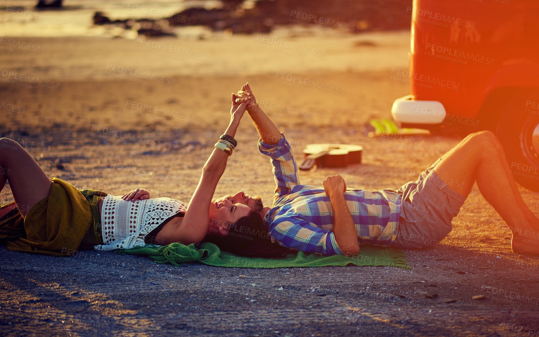 Buy stock photo Shot of an affectionate young couple holding hands while lying on the beach