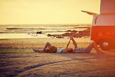 Buy stock photo Shot of an affectionate young couple holding hands while lying on the beach