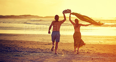 Buy stock photo Rearview shot of a young couple running towards the water on a beach