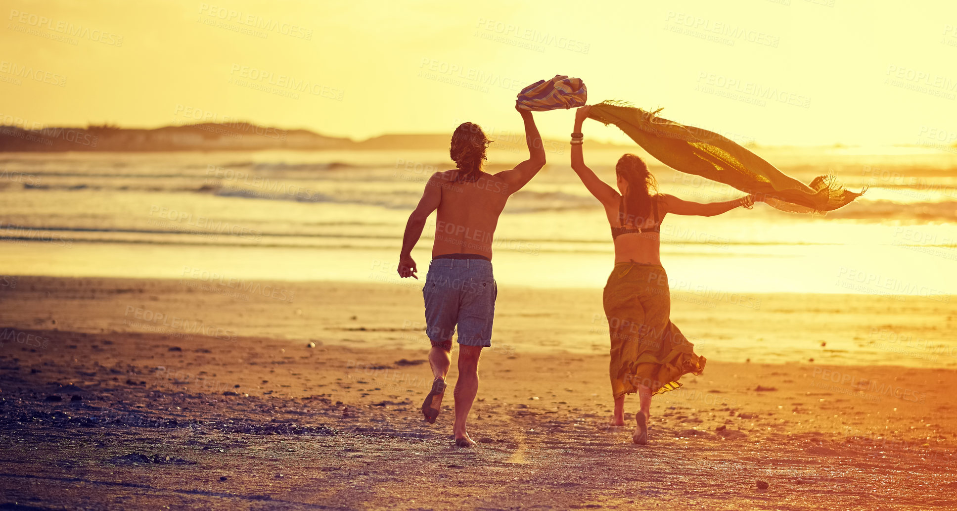 Buy stock photo Rearview shot of a young couple running towards the water on a beach