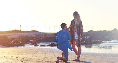 Buy stock photo Shot of a young man holding his girlfriend’s hand on bended knee at the beach