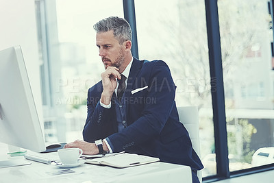 Buy stock photo Shot of a mature businessman using a computer at his desk in a modern office