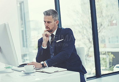 Buy stock photo Shot of a mature businessman using a computer at his desk in a modern office