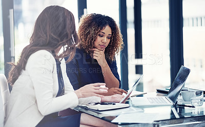 Buy stock photo Shot of two businesswomen using a digital tablet together during a collaboration at work