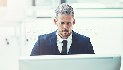 Buy stock photo Shot of a mature businessman using a computer at his desk in a modern office