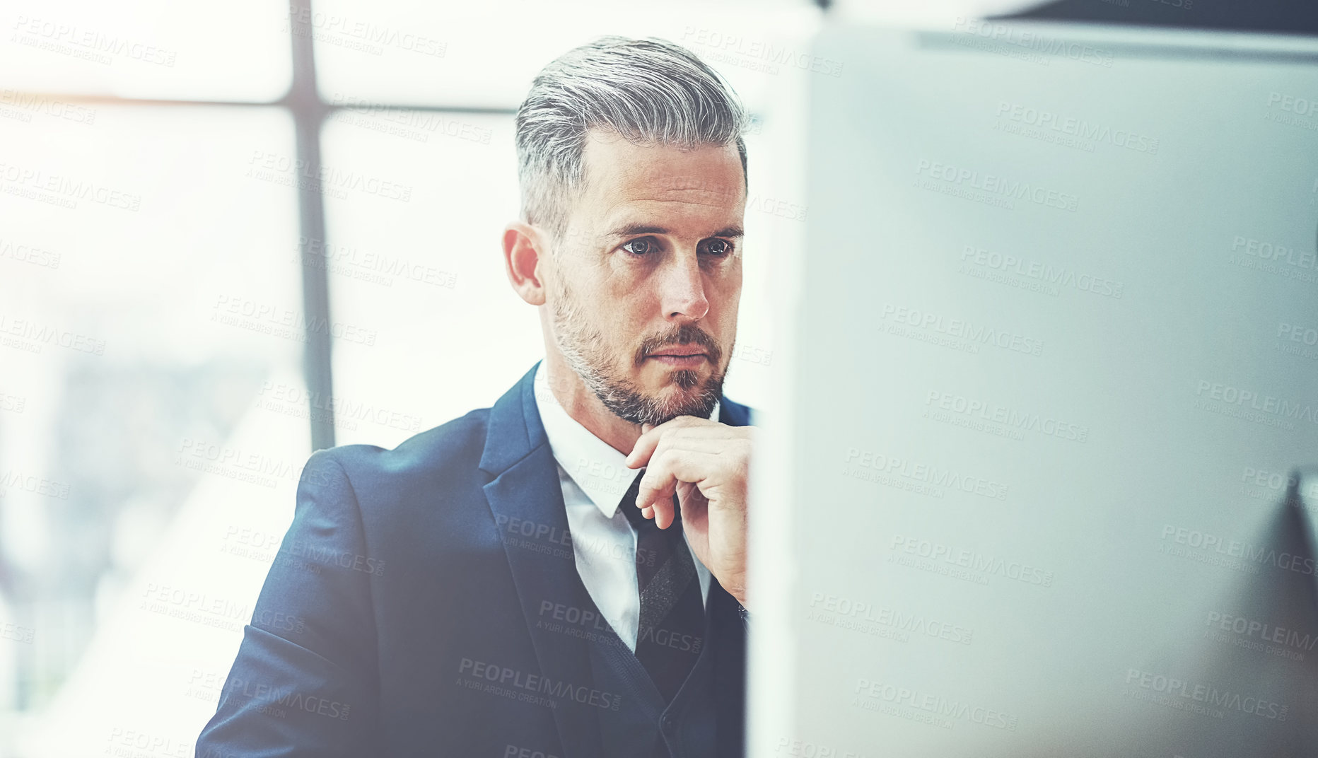Buy stock photo Shot of a mature businessman using a computer at his desk in a modern office