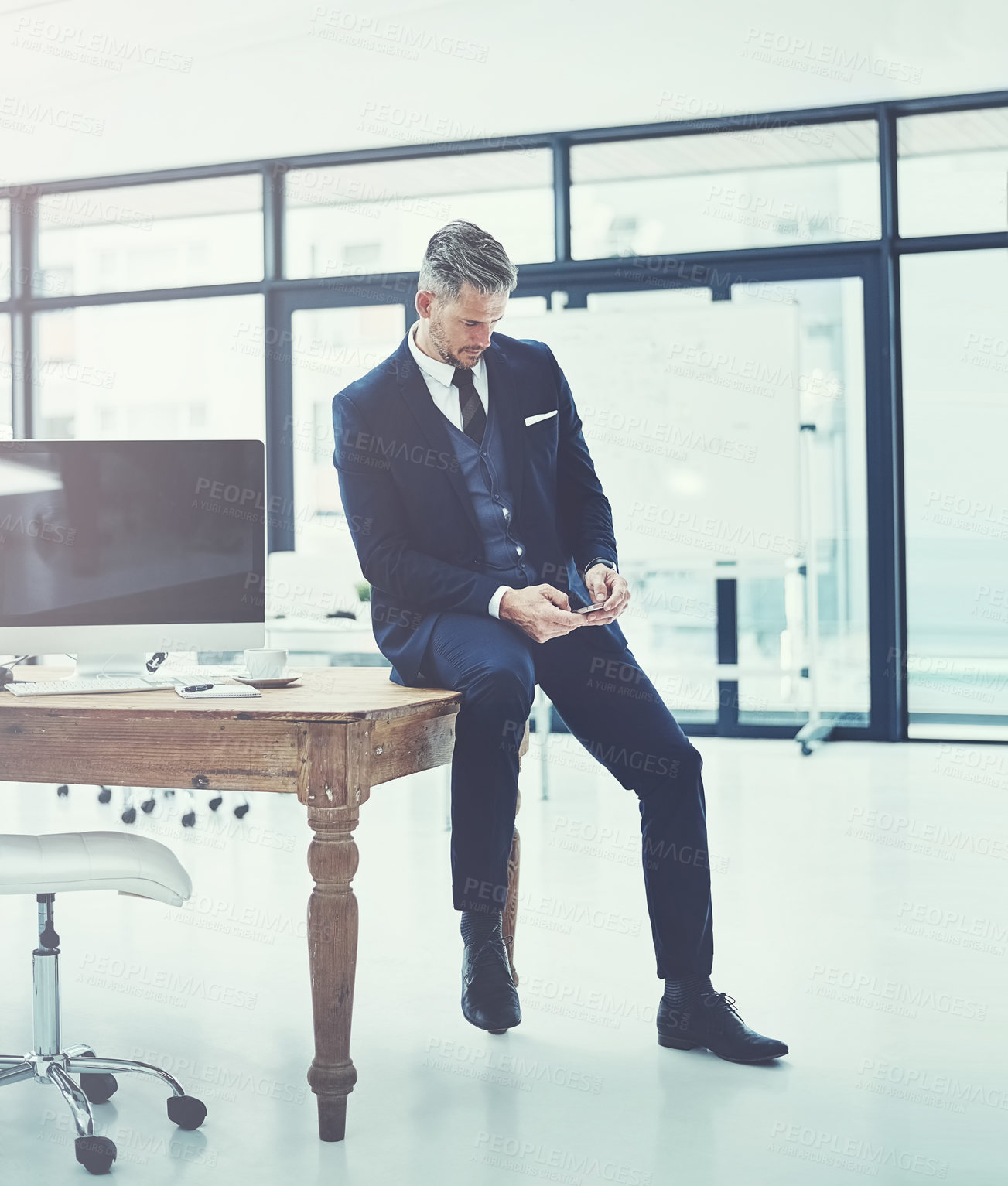 Buy stock photo Shot of a mature businessman using a cellphone at his desk in a modern office