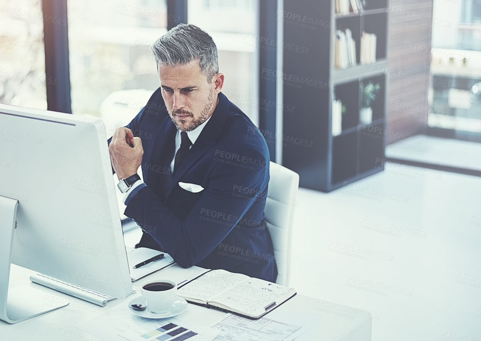 Buy stock photo Shot of a mature businessman using a computer at his desk in a modern office