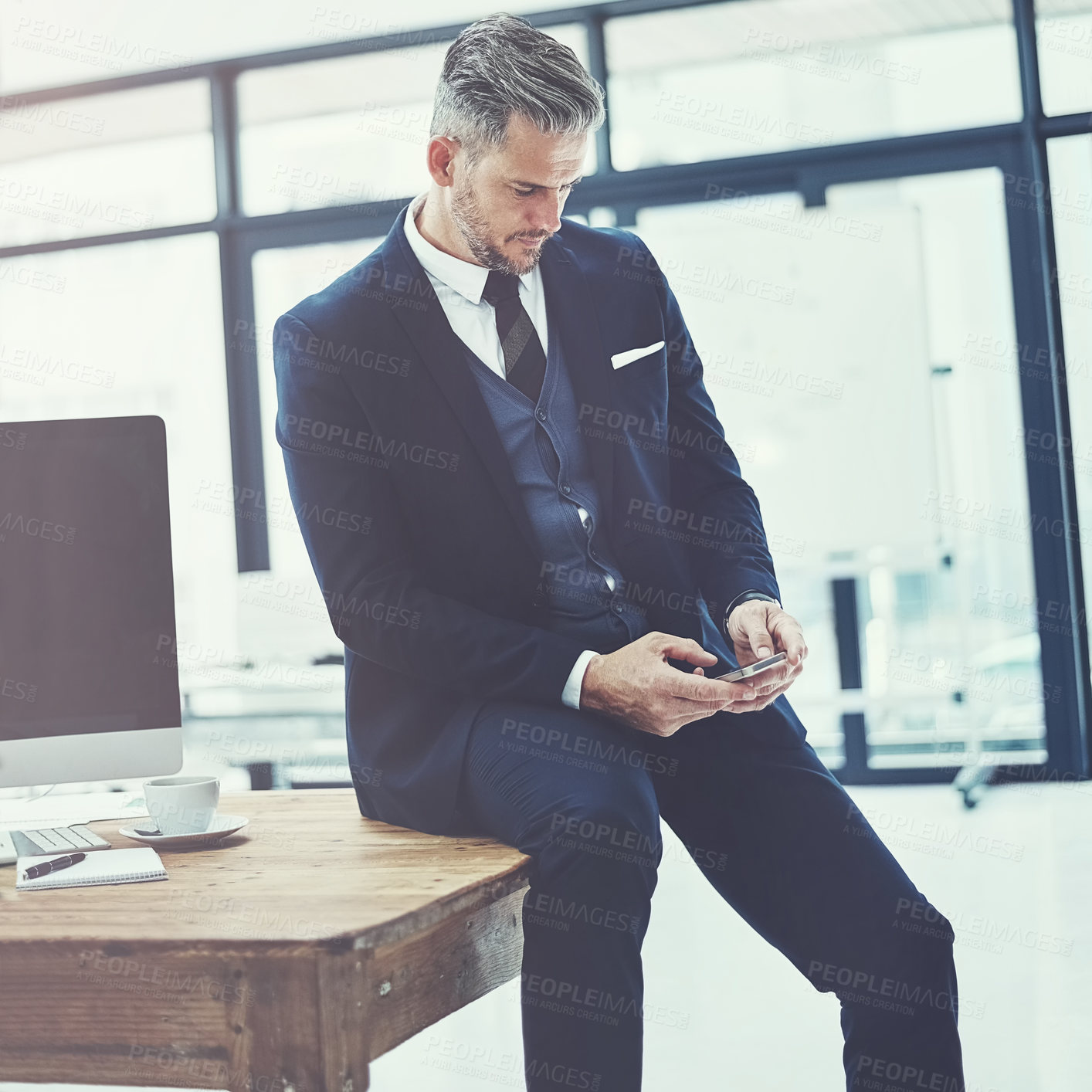 Buy stock photo Shot of a mature businessman using a cellphone at his desk in a modern office