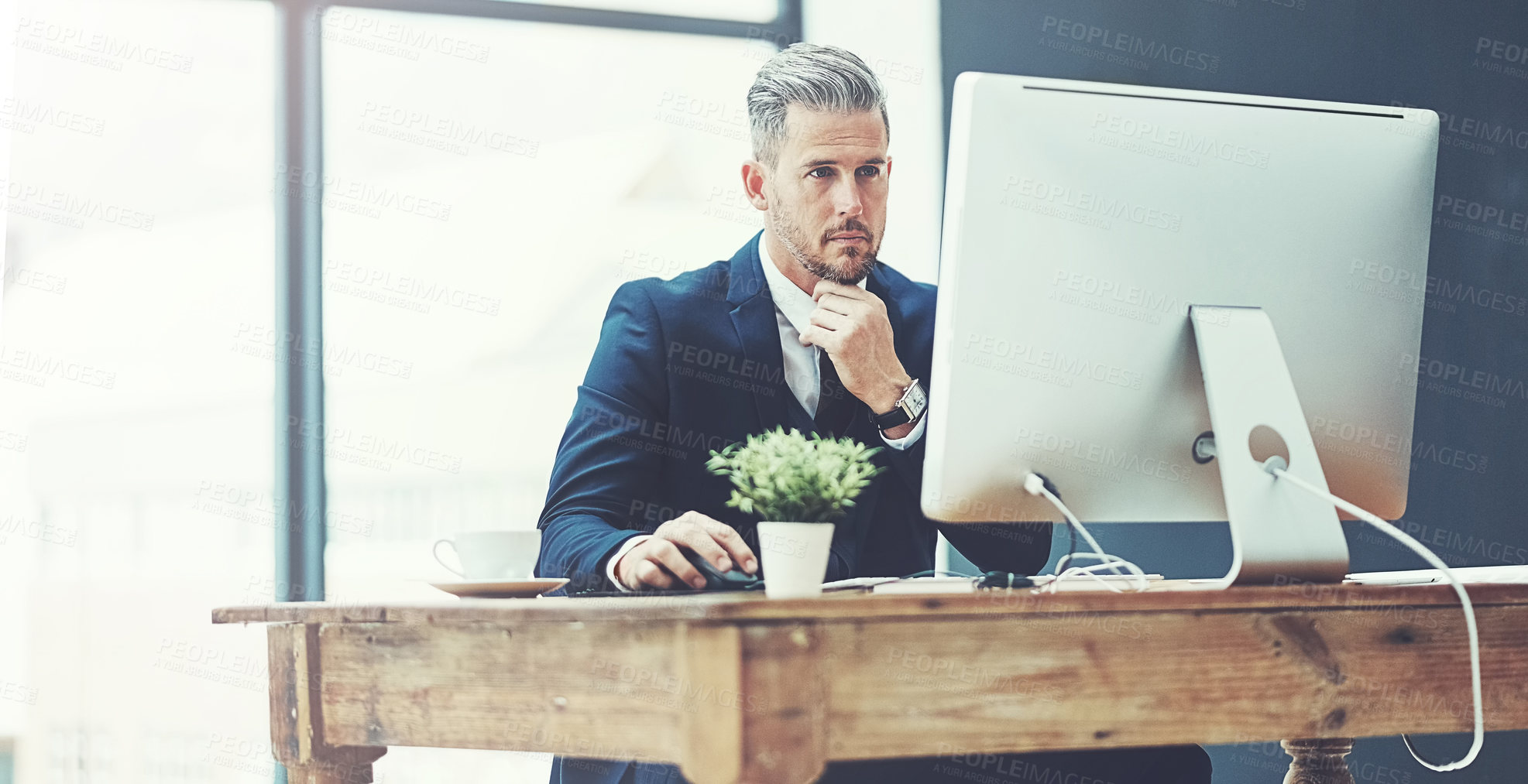 Buy stock photo Shot of a mature businessman using a computer at his desk in a modern office