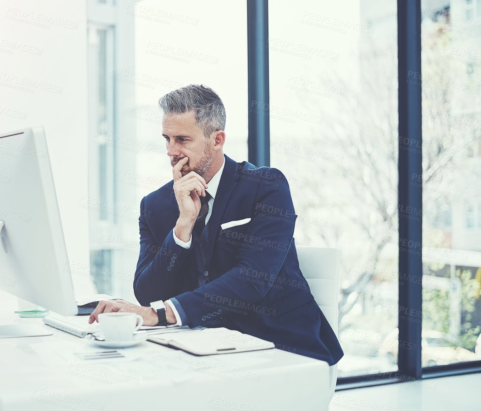 Buy stock photo Shot of a mature businessman using a computer at his desk in a modern office