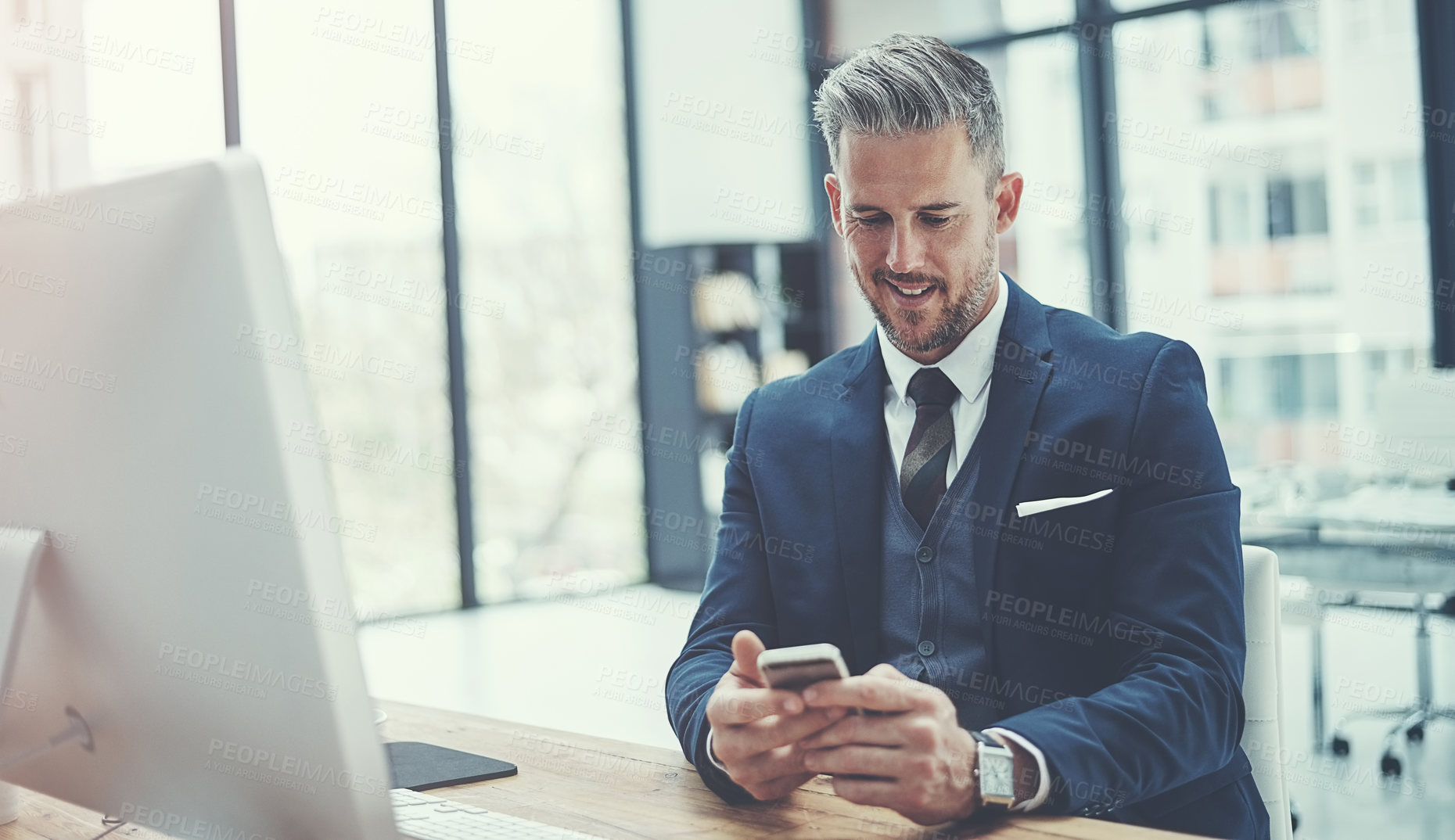 Buy stock photo Shot of a mature businessman using a cellphone at his desk in a modern office