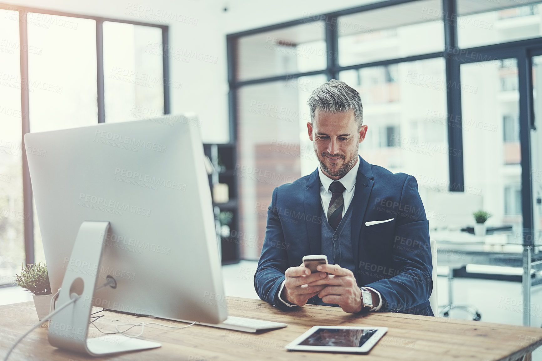 Buy stock photo Shot of a mature businessman using a cellphone at his desk in a modern office