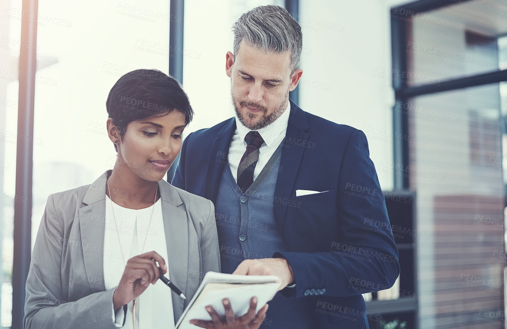 Buy stock photo Shot of a businesswoman and businessman using a notepad together at work