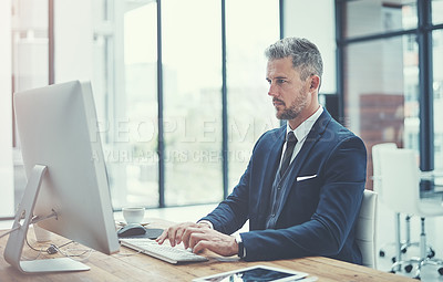 Buy stock photo Shot of a mature businessman using a computer at his desk in a modern office