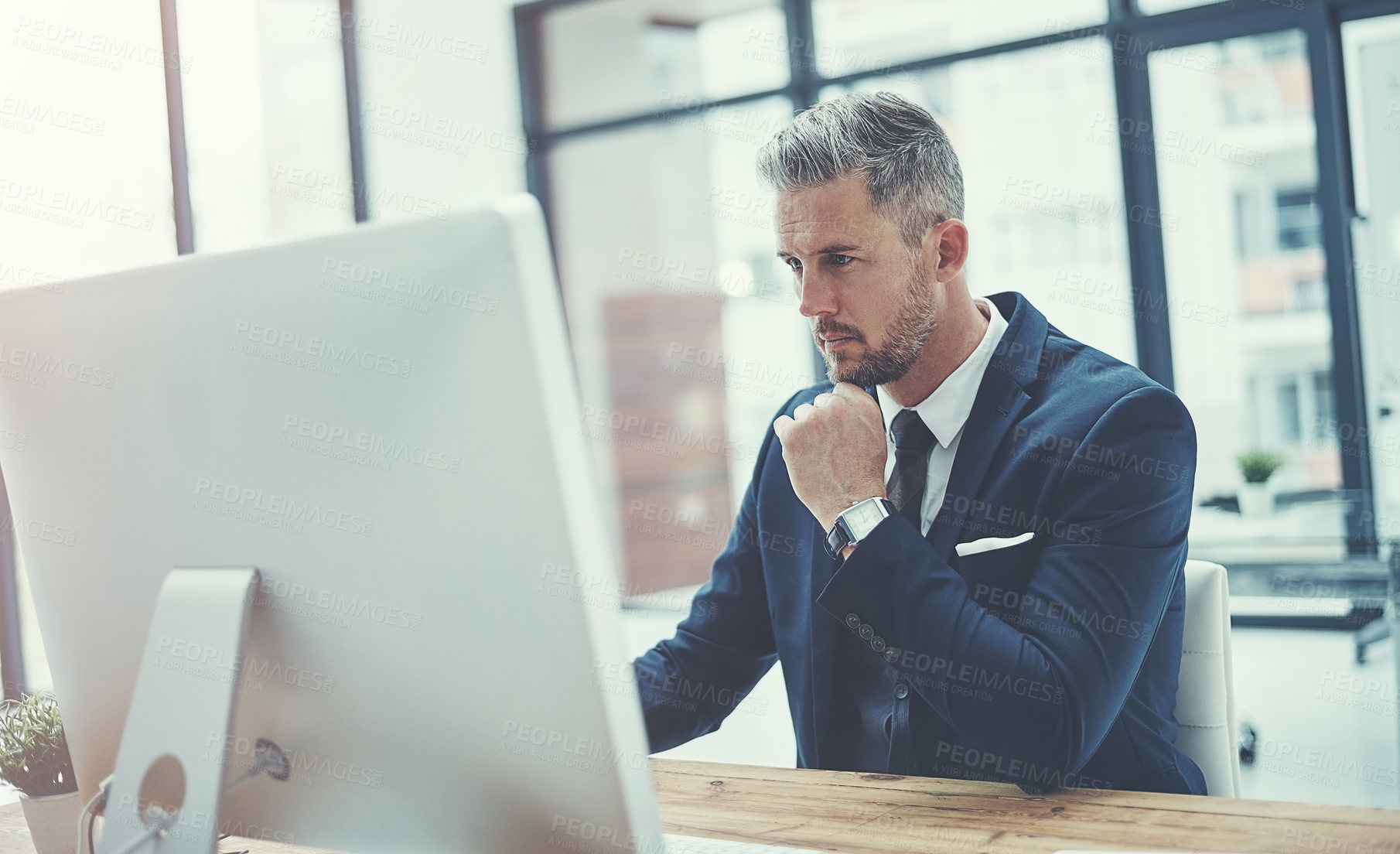 Buy stock photo Shot of a mature businessman using a computer at his desk in a modern office