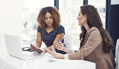 Buy stock photo Shot of two businesswomen using a digital tablet together during a collaboration at work