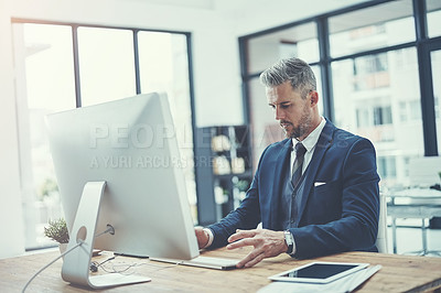 Buy stock photo Shot of a mature businessman using a computer at his desk in a modern office