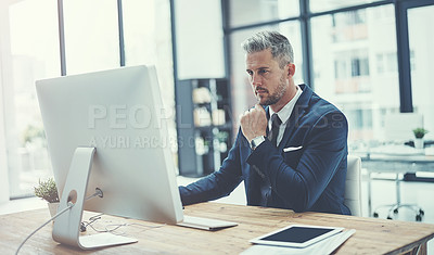 Buy stock photo Shot of a mature businessman using a computer at his desk in a modern office