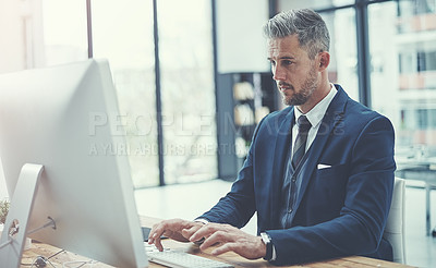 Buy stock photo Shot of a mature businessman using a computer at his desk in a modern office