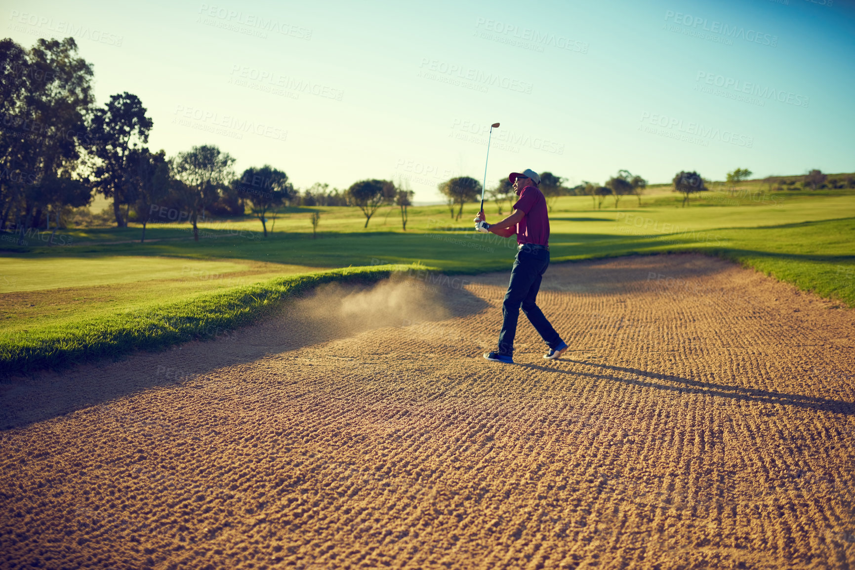 Buy stock photo Shot of a young man hitting the ball out of the bunker during a round of golf