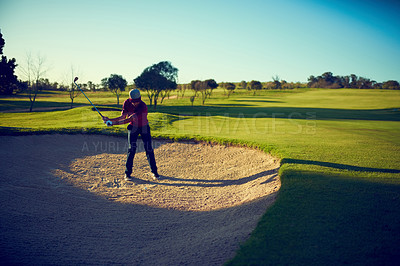 Buy stock photo Shot of a young man hitting the ball out of the bunker during a round of golf